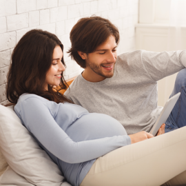 A man and pregnant lady sitting on a bed, looking at an iPad